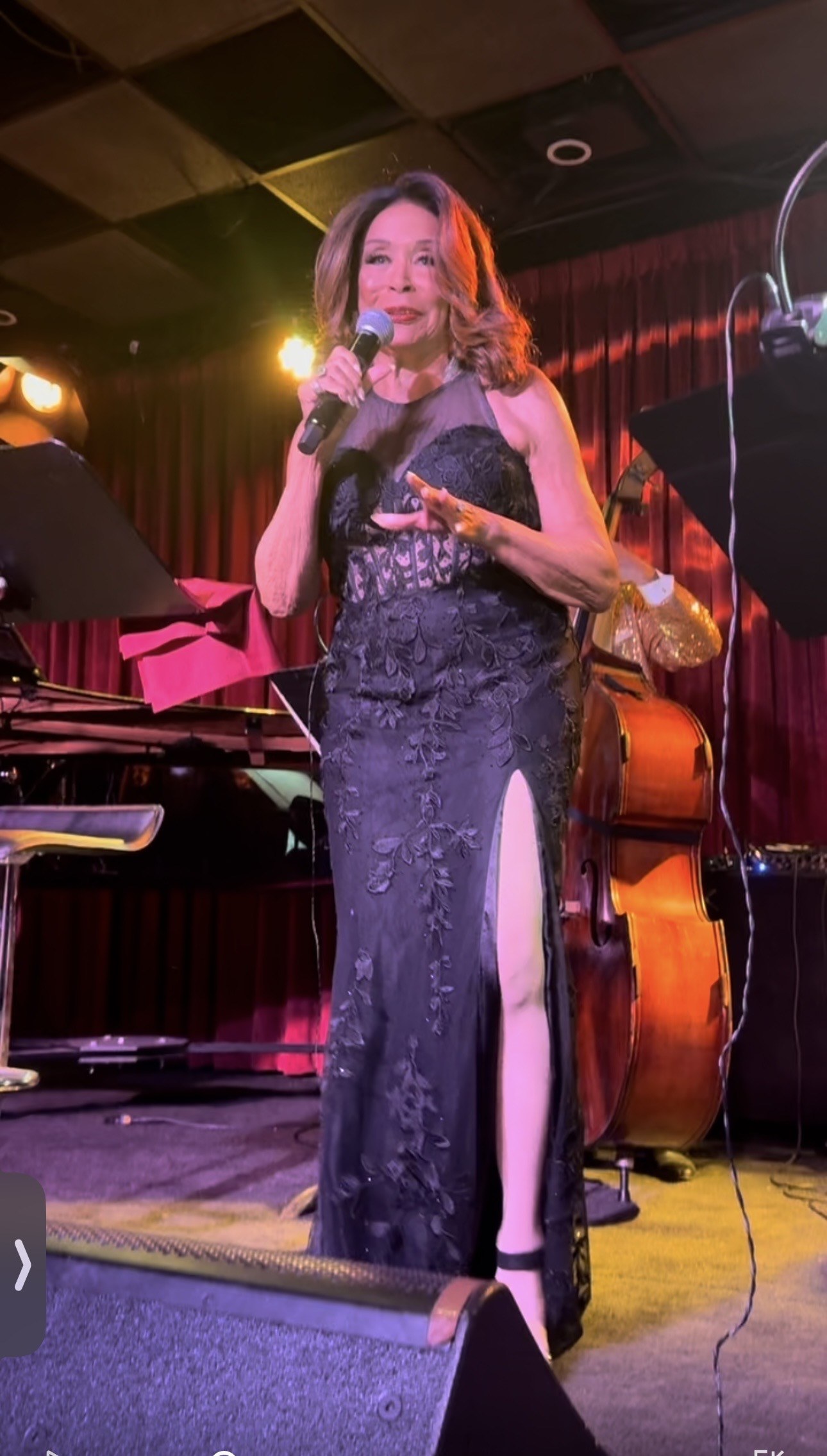 Freda Payne in a black lace gown with a thigh-high slit, an upright bass behind her